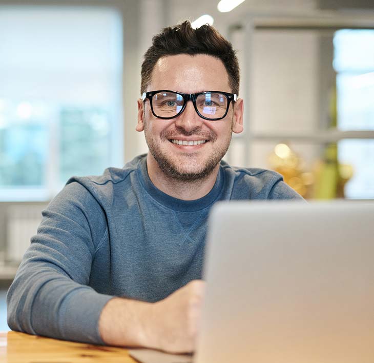 Man with Glasses Smiling Behind Laptop